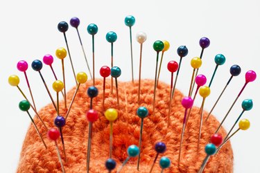 Multicolored sewing pins in the orange pin cushion on light background. Closeup, selective focus