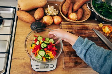 Shot of a young woman weighing a bowl vegetables