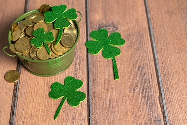 Pot full of coins next to several clovers on a wooden table. St. Patrick's Day Celebration