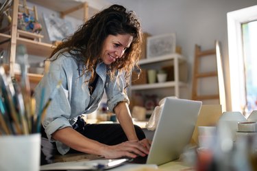 Mid adult potter woman, using laptop indoors in art studio small business concept.