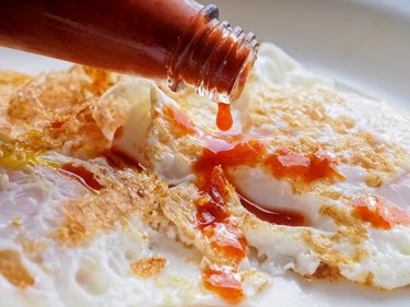 Close-up of fried eggs with spicy hot sauce being poured on top