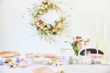 A modern table decoration as an Easter table with a floral Easter wreath hanging on the wall