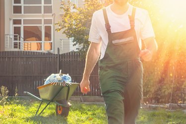 close-up of the gardener in green uniform in motion,in the background cart with bags and rakes.tint