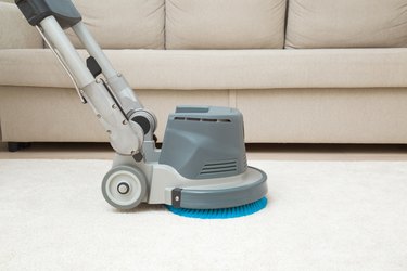 Professional disc machine on light beige carpet at home room. Closeup. Foaming and brushing equipment. Commercial cleaning service. Side view.