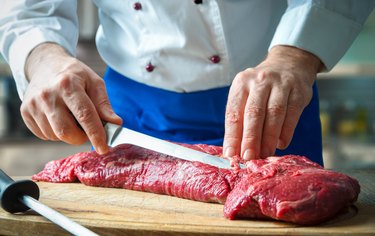 Hands of male chef in uniform cutting big piece of beef