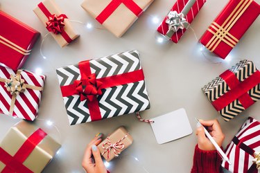 Top view of anonymous woman with sweater writing on blank label of Christmas gift during holiday celebration on gray background. New Year celebration concept