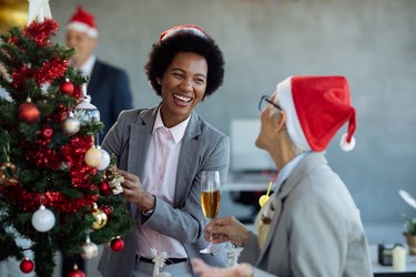 Cheerful black businesswoman and her colleague having fun while decorating Christmas tree in the office.