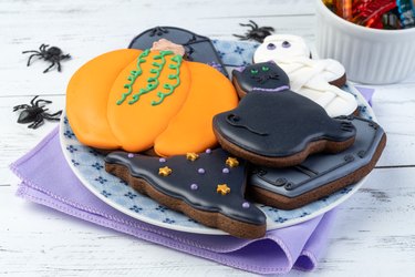 Halloween gingerbreads, pumpkin, tombstone, witch hat, black cat on a plate over wooden table