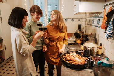Three women drinking wine while preparing christmas dinner at home