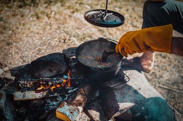 Stirring food in a cast-iron Dutch oven over a campfire