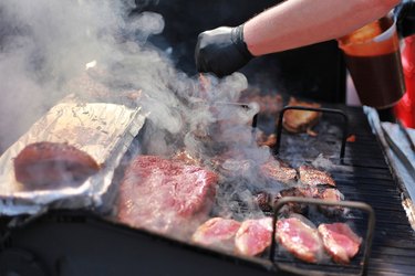 Close up shot of cook grilling smoking beef steak outdoors.