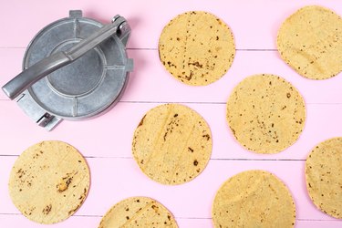 Metallic manual machine tortilla press on pink background