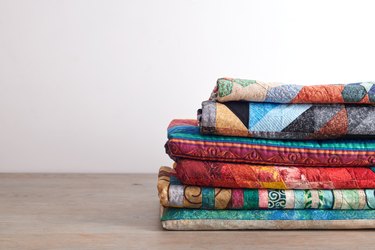 Quilts stacked on wooden table on white wall background