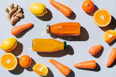 Ginger, carrots, lemons and ginger alongside bottled orange-hued juices against a light blue background