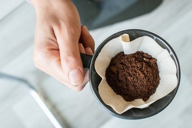 Cropped shot view of barista hand holding a cup with ground coffee inside with paper filter before drip it.