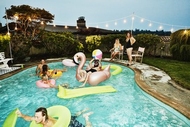 Smiling and laughing group of friends having backyard pool party on summer evening