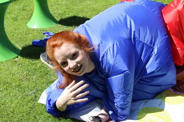 Image of red haired teenage girl 14 / 15 playing outdoors in the garden on sunny day, playing physical skill game wearing blue inflatable sumo fatsuit