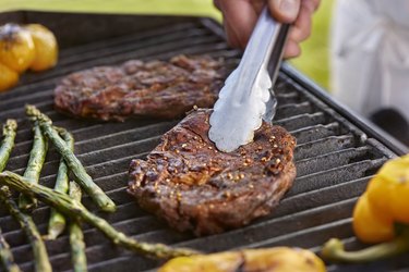 Grilling seasoned rib eye steaks, yellow bell peppers and asparagus spears on the BBQ