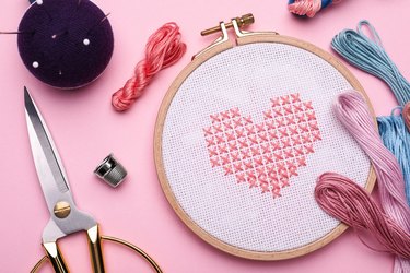 Flat lay composition with embroidery and different sewing accessories on pink background