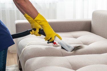 Close-up of housekeeper holding modern washing vacuum cleaner and cleaning dirty sofa with stain with professionally detergent. Professional springclean at home concept