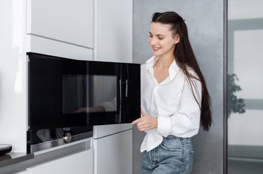 Happy woman opening black microwave door in kitchen
