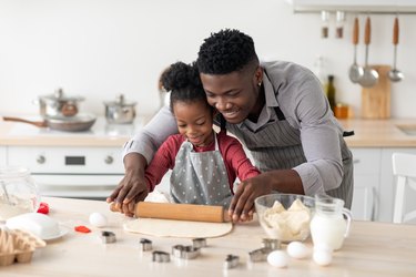 Loving black father rolling pastry dough with daughter