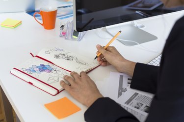 Woman drawing into notebook at desk in office