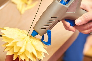 Woman make floral design. Girl glues the petals of an artificial flower using a glue gun. Close-up, selective focus