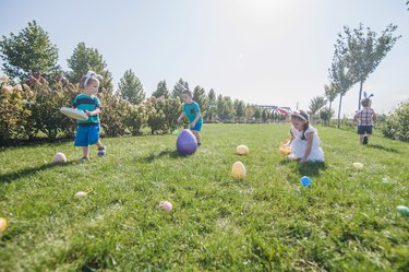 Easter tradition of searching eggs in grass. Children Easter egg hunters with baskets and hare ears.