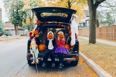 Trick or trunk. Children celebrating Halloween in trunk of car. Boy and girl with red pumpkins celebrating traditional October holiday outdoors. Social distance during coronavirus covid-19.