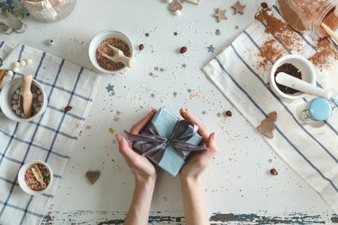 Cropped Hands Of Woman Holding Gift Box On Table