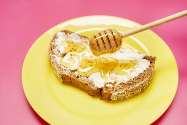 Honey dipper drips honey onto bread slice on yellow plate