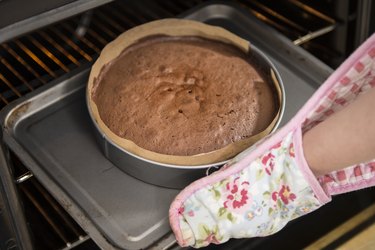 Close up of female hands removing cake from oven in bakery