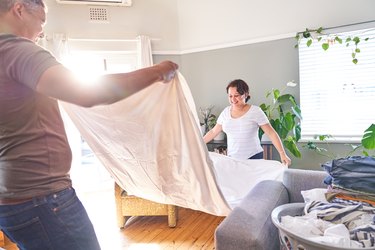 Smiling couple folding sheets in sunny living room