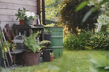 Gardener work bench (potting table) in summer garden with rainwater barrel. Wooden rustic style house, different tools and pots.