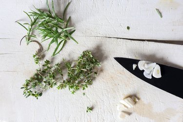 Herbs and garlic on white cutting board with black knife