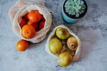 Organic tangerines and pears in a reusable mesh bag on the kitchen countertop