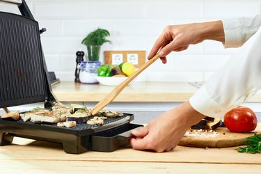 Woman holding spatula for cooking and serving barbecue on table. Grill steak on an electric stove at kitchen.