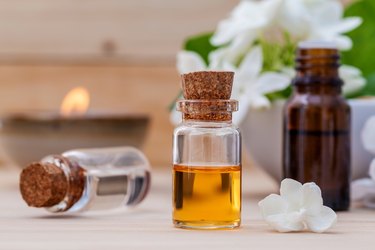 Bottle of essential oil and jasmin flower with shallow depth of field setup on wooden background .