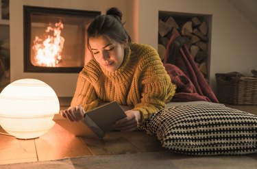 Young woman reading book at the fireplace at home