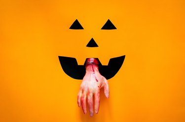 Halloween pumpkin face background with bloody hand on black and orange paper