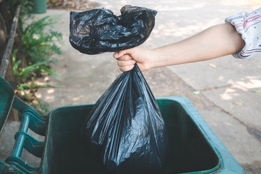 Cropped Hand Of Woman Putting Plastic Bag In Dustbin