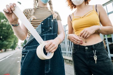 Young women wearing masks, holding roll of tape