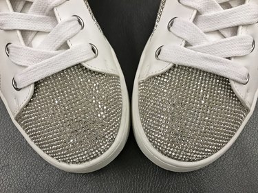 Pair of white sneakers with glittering plastic rhinestones on black background