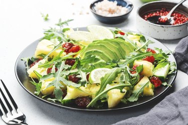 Summer vegan salad with juicy pineapple, fresh arugula, avocado and dried cranberry on white stone kitchen table, top view. Healthy eating, clean diet food, weight loss concept