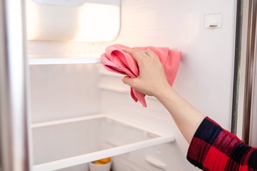 Woman cleans up the shelves in the fridge with pink cloth.