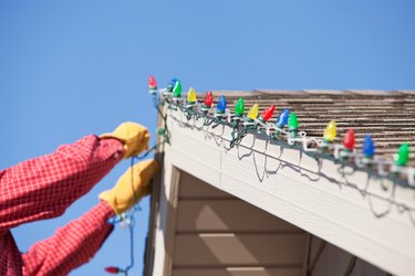 Gloved Hands Installing LED Christmas Light on House Roof