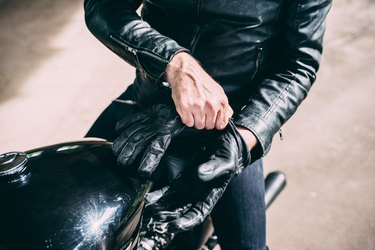 Mid section of male motorcyclist sitting on motorcycle putting on gloves
