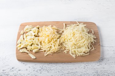Wooden board with three types of grated cheese on a light background