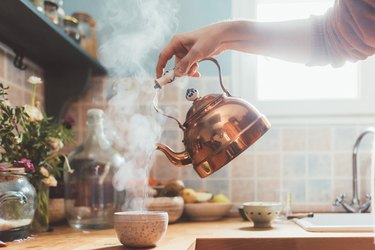 Arm pouring boiling water into bowl in kitchen